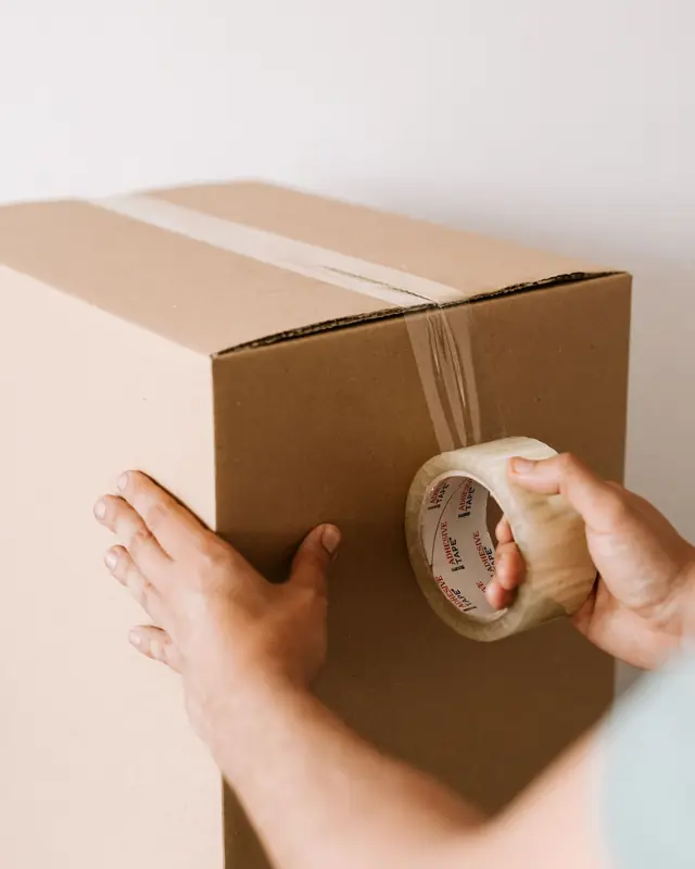Hands sealing a cardboard box with clear packing tape